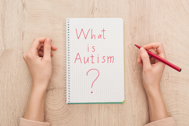 cropped view of woman holding marker near notebook with what is autism question on wooden table - Photo, Image