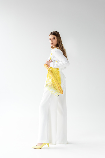 young woman holding yellow string bag with baguette and bottle of milk on white  - Fotografie, Obrázek