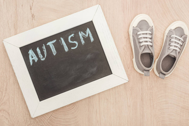top view of autism lettering written on chalkboard near children grey sneakers on wooden surface - Photo, Image
