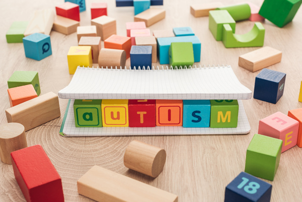 autism lettering made of multicolored cubes in notebook among building blocks on wooden surface - Foto, Imagem