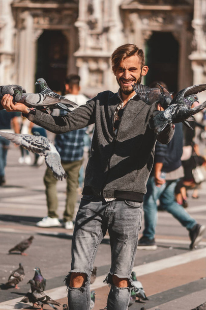 Boldog fiatalember jelentő galambok a milánói utcában ősi templom Duomo di Milano a háttérben. Aranyos boldog 23 éves öreg pózol, Milánó, Olaszország. - Fotó, kép