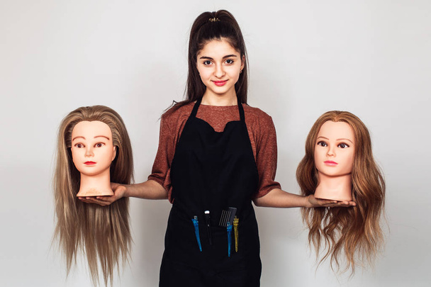 молодая девушка парикмахер держит в руках две головы манекена
. - Фото, изображение
