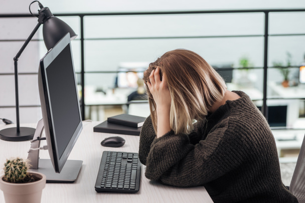 upset girl sitting at workplace with hands on head in modern office - Foto, Imagem