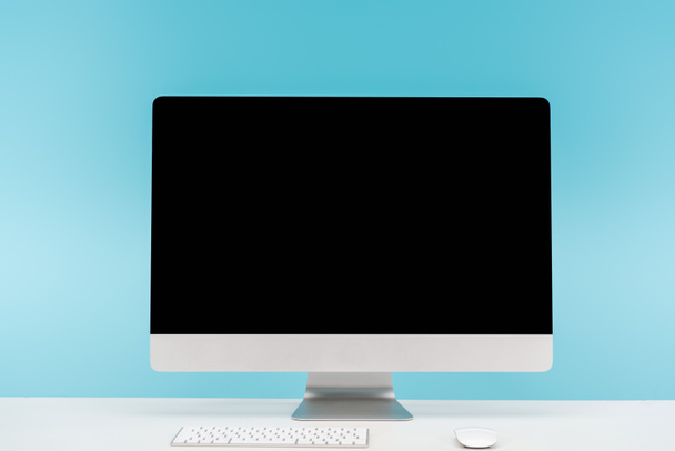 local de trabalho com monitor de computador, teclado e mouse de computador na mesa branca no fundo azul
 - Foto, Imagem
