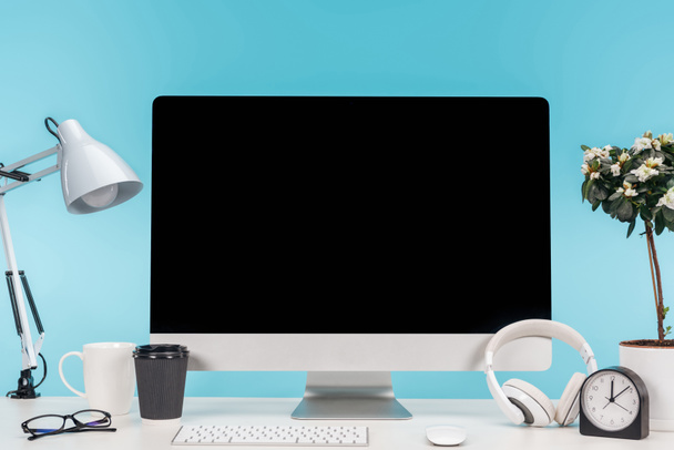 työpaikka tietokone, lamppu, kuppi, kahvi mennä, kello ja kukkaruukku valkoisella pöydällä sinisellä pohjalla
 - Valokuva, kuva