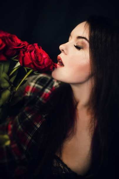 young and beautiful woman posing with red roses against black background - Fotó, kép