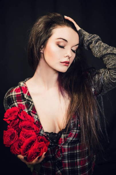 young and beautiful woman posing with red roses against black background - Foto, Bild