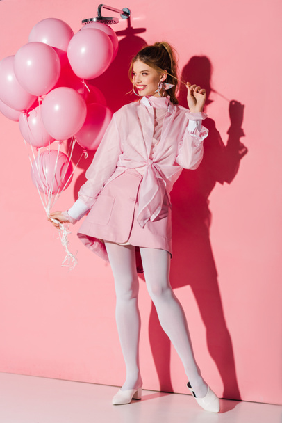 alegre joven mujer sosteniendo globos de aire mientras toca el pelo en rosa
 - Foto, imagen