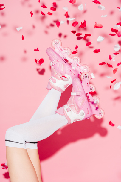 cropped view of girl wearing long socks and roller-skates near rose petals on pink - Fotografie, Obrázek