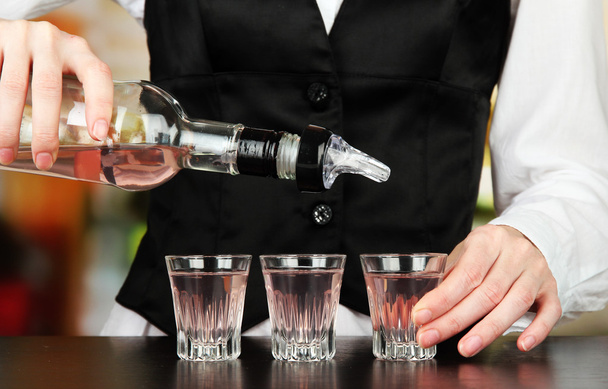 Barmen hand with bottle pouring beverage into glasses, on bright background - Photo, Image
