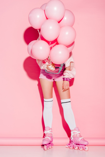 mulher cobrindo rosto com balões de ar, enquanto em pé em patins em rosa
 - Foto, Imagem
