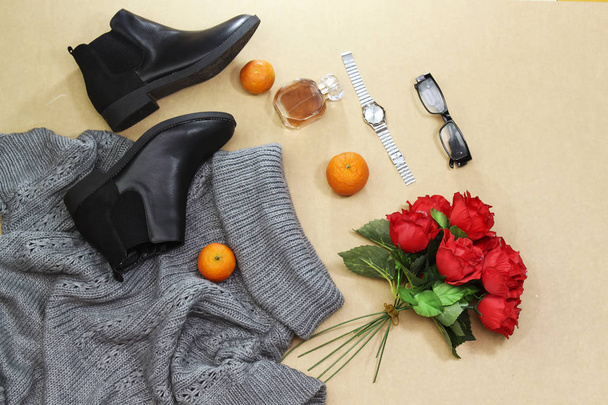 Conjunto de ropa de invierno de otoño para mujer: jersey gris de gran tamaño, botas negras y bufanda, frasco de perfume de vidrio, reloj de mano plateado, anteojos, fruta naranja. Ropa de moda para paseos, cama plana
 - Foto, Imagen