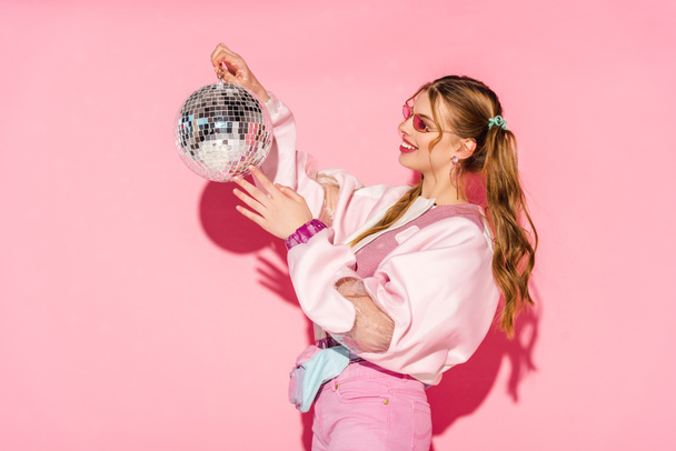 cheerful young woman looking at disco ball on pink - Photo, Image