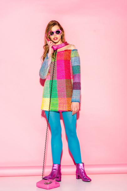 young woman in sunglasses and checkered dress talking on retro phone on pink - 写真・画像