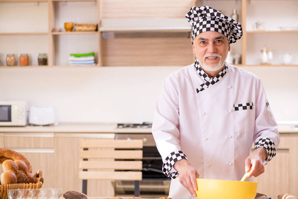Old male baker working in the kitchen - Foto, imagen