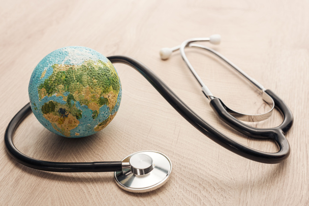 selective focus of stethoscope and toy earth on wooden and white table  - Foto, Imagem