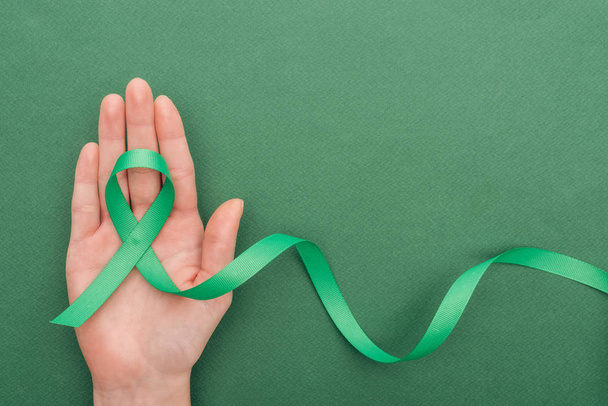 cropped view of woman holding green ribbon on green background with copy space   - Photo, image