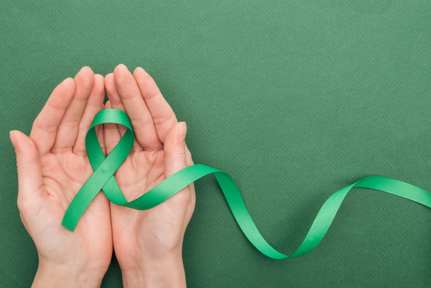 cropped view of woman holding green ribbon on green background with copy space   - Fotografie, Obrázek