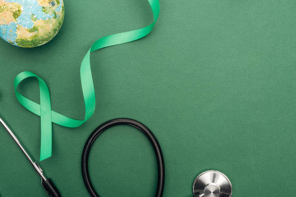 top view of green ribbon, toy earth and stethoscope on green background  - Фото, зображення