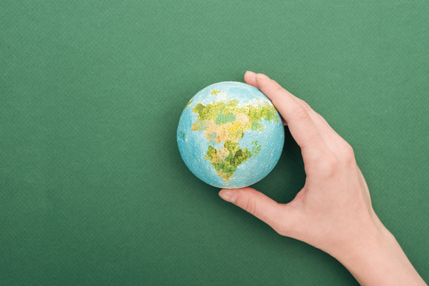 partial view of woman holding toy earth on green background with copy space - Foto, immagini