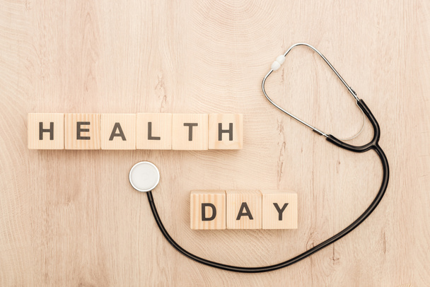 top view of cubes with health day lettering and stethoscope on wooden background  - Foto, afbeelding