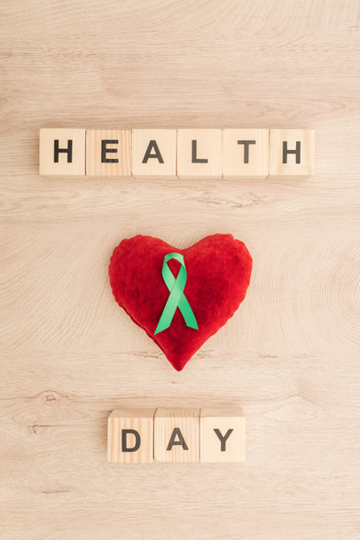 top view of cubes with health day lettering, toy heart and green ribbon on wooden background  - Fotó, kép