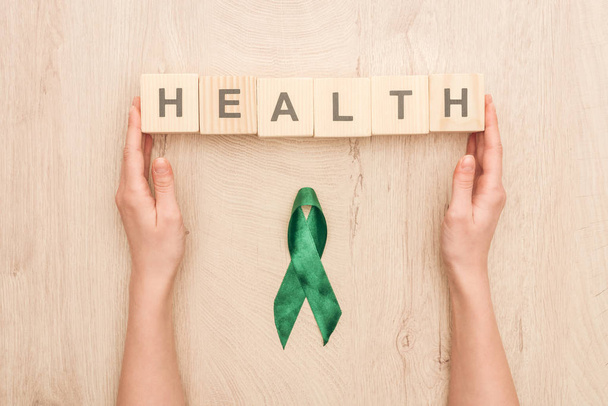 partial view of woman holding cubes with health lettering and green ribbon on wooden background  - Foto, immagini