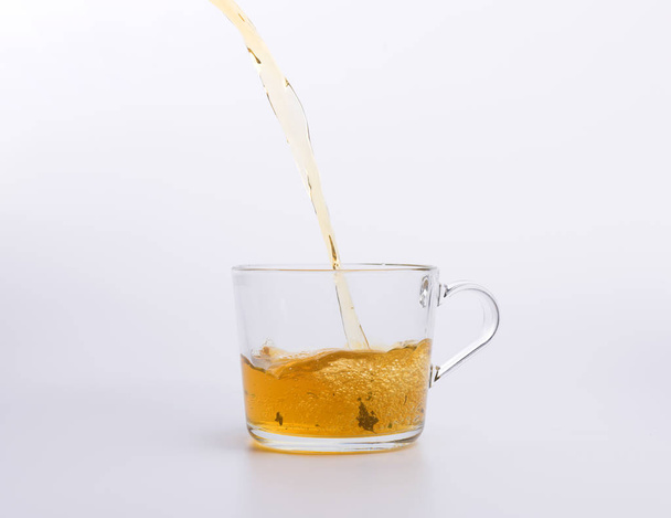 Чай наливається в скляну чашку ізольовано на білому
 - Фото, зображення
