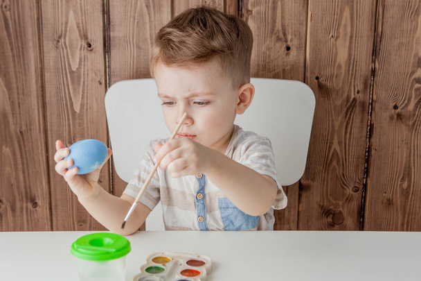 Little boy painting colorful eggs for easter on wooden background - Photo, image