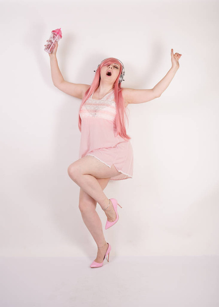 Sexual super plump redhaired girl wearing pink lingerie babydoll dress with headphones and having cosplay fun on white studio background - 写真・画像