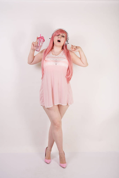 Sexual super plump redhaired girl wearing pink lingerie babydoll dress with headphones and having cosplay fun on white studio background - Φωτογραφία, εικόνα