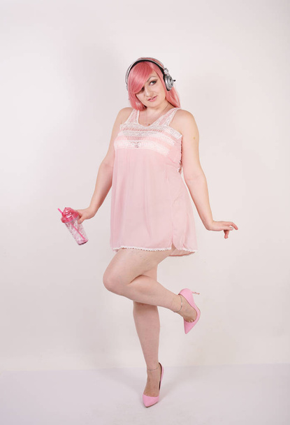 Mujer bastante adulta con cuerpo regordete usando lencería babydoll vestido rosa con tacones y de pie sobre fondo blanco estudio solo
 - Foto, imagen