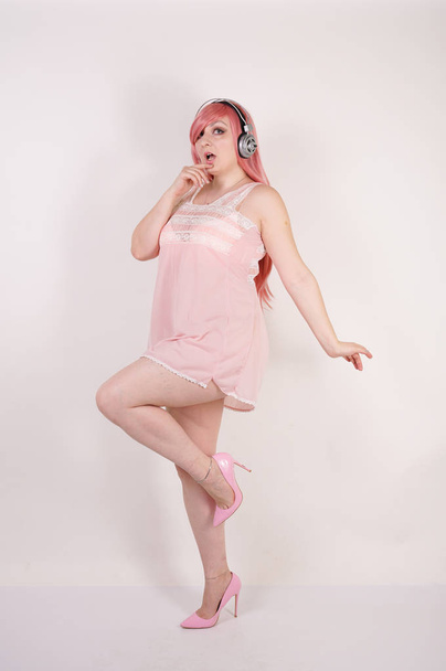Красивая взрослая женщина с пухлым телом в розовом платье с каблуками и на белом фоне студии одна
 - Фото, изображение