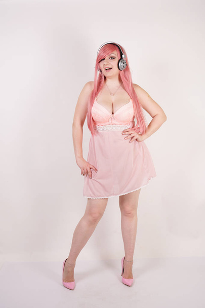 сексуальна пухнаста руда дівчина в рожевій сукні для бабідолів з навушниками та косплей весело на білому фоні студії
 - Фото, зображення