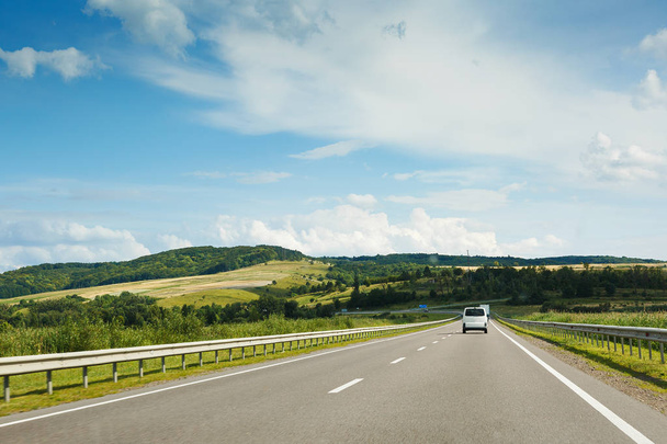 Pusty asfaltu drogowego i niebieski niebo z białe chmury w słoneczny dzień. Klasyczny widok drogi przez pola i wzgórza  - Zdjęcie, obraz