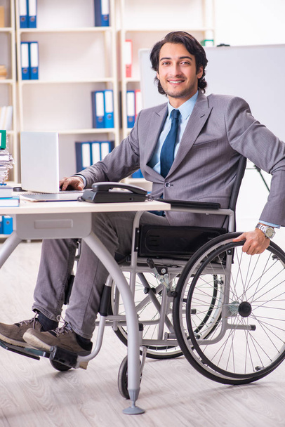 Молодой красивый работник в инвалидной коляске в офисе
 - Фото, изображение