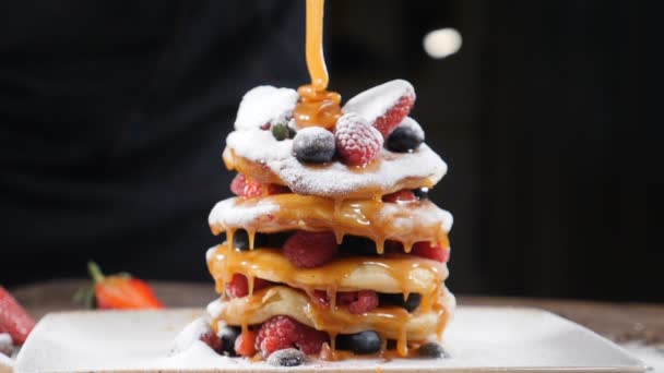 Cooking art. Chef spreading caramel on top of stack of fresh fluffy pancakes decorated with forest berries. Homemade Healthy Vegan Fluffy American Style Pancakes with Fresh Fruits. Pouring honey on - Кадри, відео
