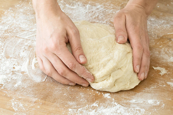 γυναικεία χέρια Ζυμώστε τη ζύμη σε ένα ξύλινο ταμπλό μαγείρεμα ψησίματος - Φωτογραφία, εικόνα