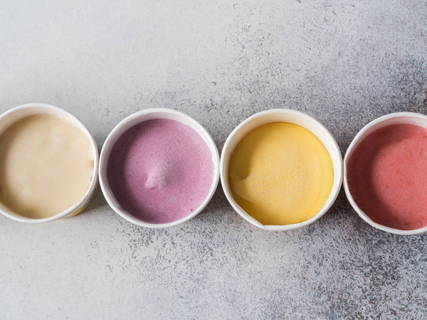 Fresh fruit ice cream of different colors in paper cups on a gray background. Top view. copy space - Foto, Imagen
