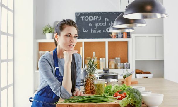 Happy young woman in kitchen with fresh vegetables on the table - Photo, Image
