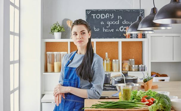 Ευτυχισμένος νεαρή γυναίκα στην κουζίνα με φρέσκα λαχανικά στο τραπέζι - Φωτογραφία, εικόνα