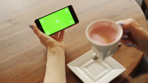 Женщина пьет чашку кофе держа мобильный телефон с зеленым экраном в другой руке
. - Кадры, видео