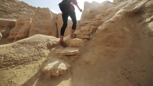 Benen van de vrouw lopen op grote woestijn stenen. Vrouw klimt op woestijn rotsachtige heuvel. Achteraanzicht. - Video