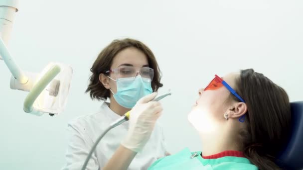 La dentista blanquea los dientes de la paciente. Medios. Odontóloga profesional limpia los dientes de las pacientes antes de blanquear con nuevos equipos estériles de estomatología
 - Metraje, vídeo