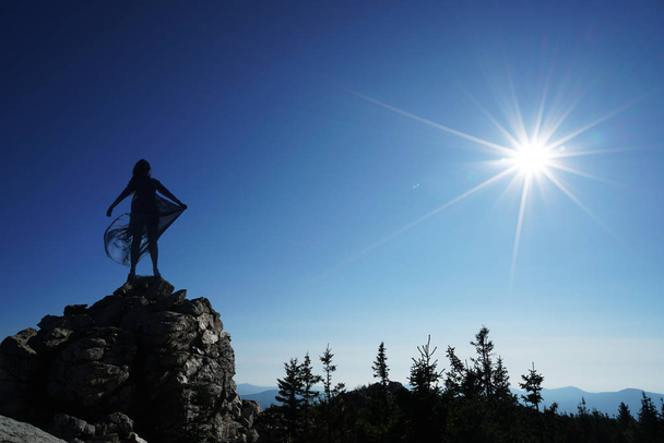 silhoutee από γυναίκα να στέκεται στην κορυφή του βουνού. Οι ακτίνες του ήλιου πέρα από το βουνό - Φωτογραφία, εικόνα