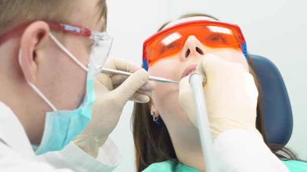 Close-up van jonge tandarts met behulp van boor en spiegel voor tanden behandelen van vrouwelijke jonge patiënt bij de tandheelkundige kantoor. Tandheelkundige zorg. - Video