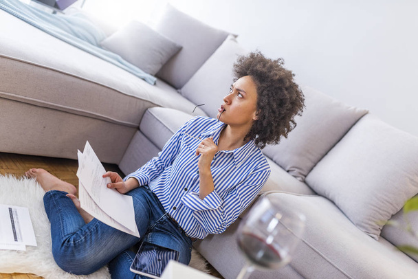 Mujer joven sentada en el suelo en casa y leyendo documentos
 - Foto, Imagen