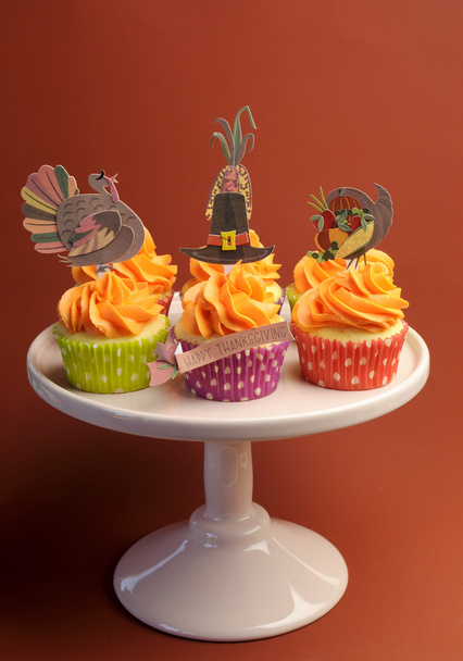 Счастливый День Благодарения украшенные кексы с индейкой, шляпа паломника и кукурузные топперы на торте стенд на коричневом фоне. Вертикаль
 - Фото, изображение