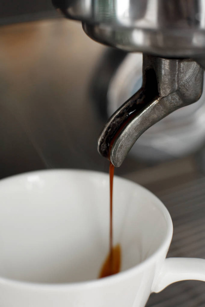 Close-up of freshly brewed coffee is poured from a coffee machine into a white cup - Photo, Image