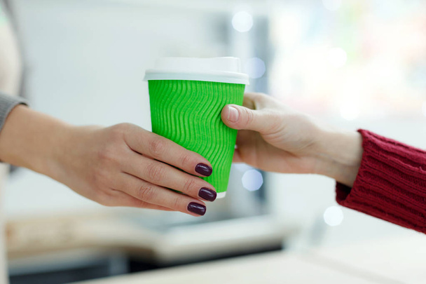 Barista in apron is giving hot coffee in green takeaway paper cu - Фото, изображение